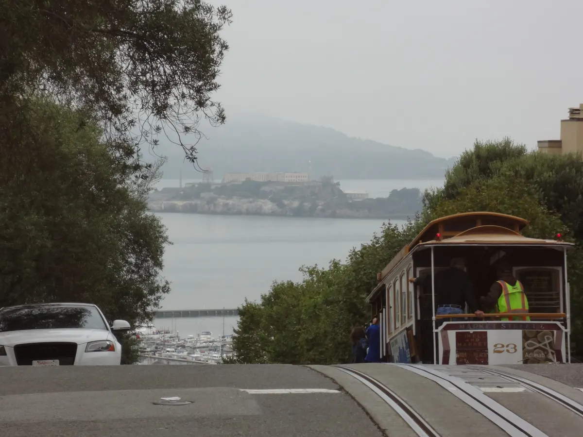 A cable car descending Hyde Street in San Francisco, with Alcatraz Island across the bay in the distance