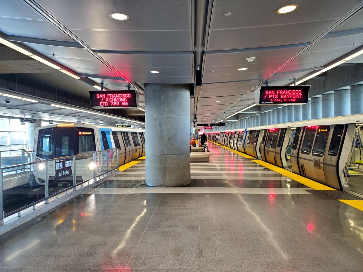 Two modern BART trains alongside the platforms at San Francisco International Airport station